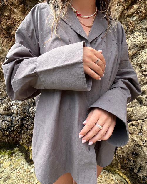Woman wearing a grey oversized shirt standing against a rocky background at the beach